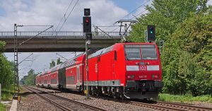 Rote Lokomotive mit angehängten Personenwagen hat gerade eine Brücke passiert